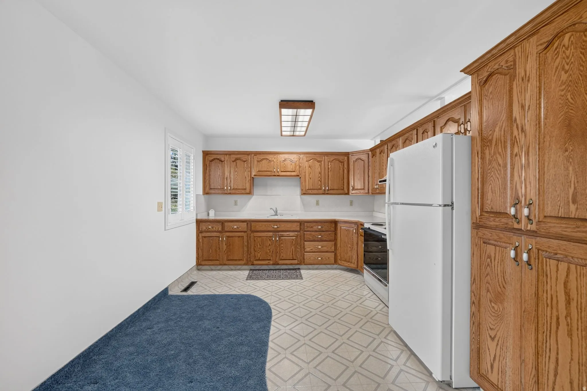 Kitchen featuring wood cabinetry, white countertops, window with shutters, and patterned flooring