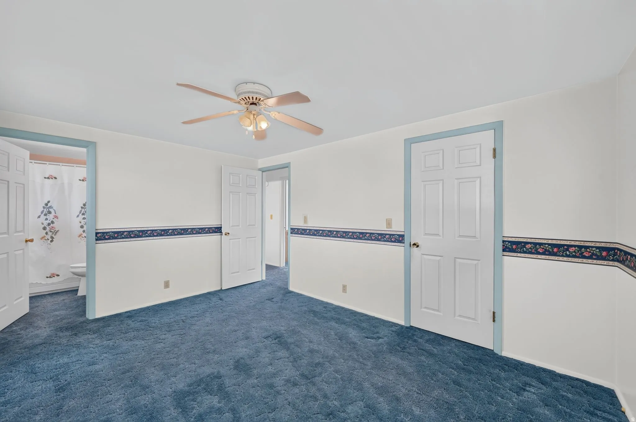 White walls with decorative border, blue carpeting, and a ceiling fan with integrated lighting