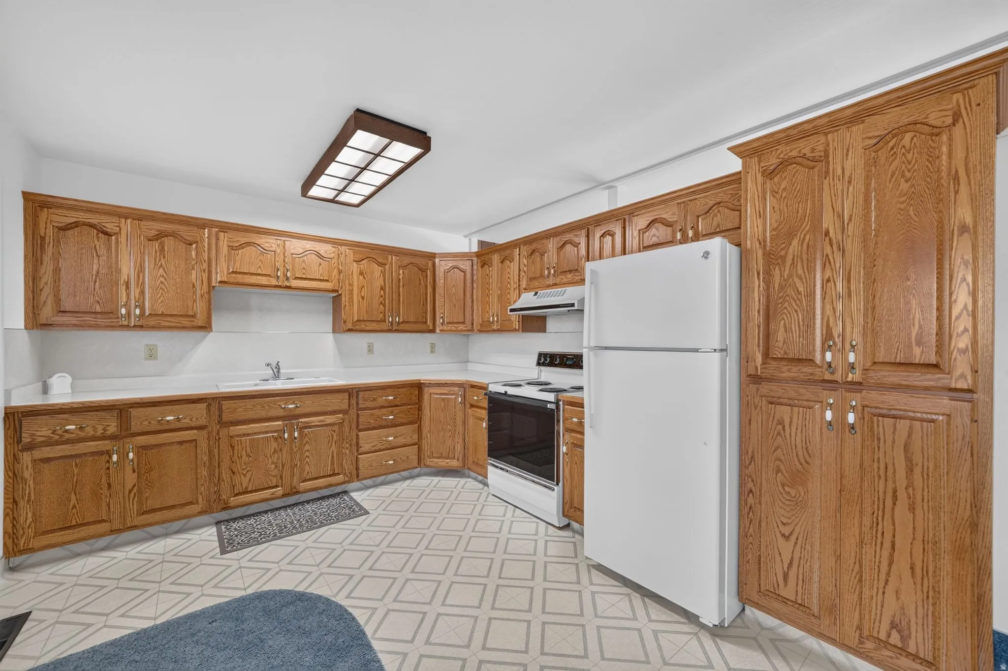 Kitchen featuring extensive wood cabinetry, white countertops, a white refrigerator, a built-in oven with cooktop, and patterned flooring