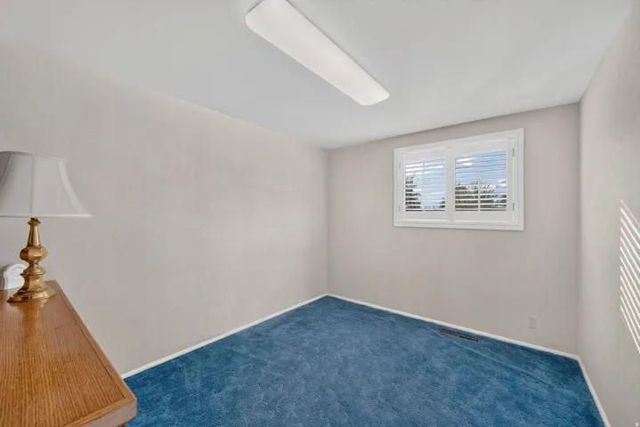 Recessed window with white plantation shutters, light-colored walls, and blue carpeting