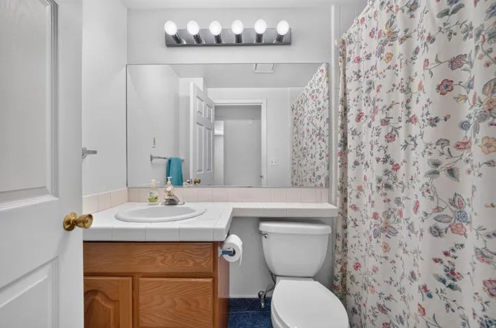 Vanity with natural wood-finish cabinetry, tile countertop with an integrated sink, and an expansive wall-mounted mirror
