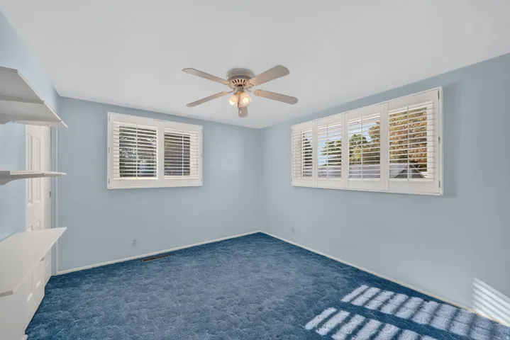 Expansive wall with white plantation shutters, two windows, and a ceiling fan with integrated lighting