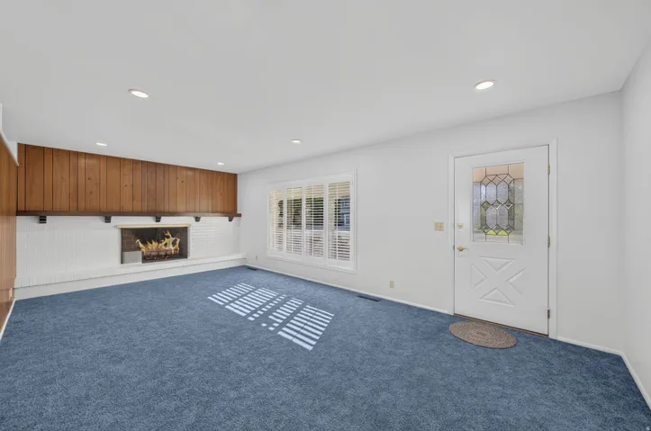 Recessed lighting, wood paneling, white brick fireplace, decorative entry door with leaded glass, and window with plantation shutters