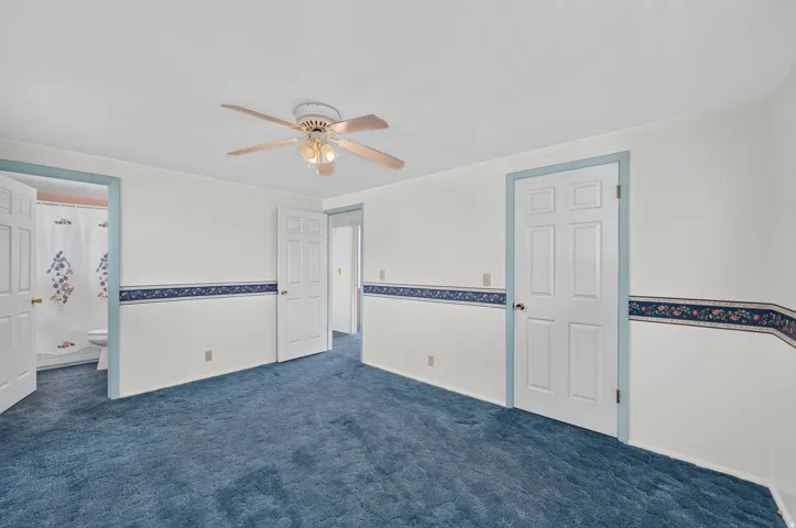 White walls with decorative border, blue carpeting, and a ceiling fan with integrated lighting