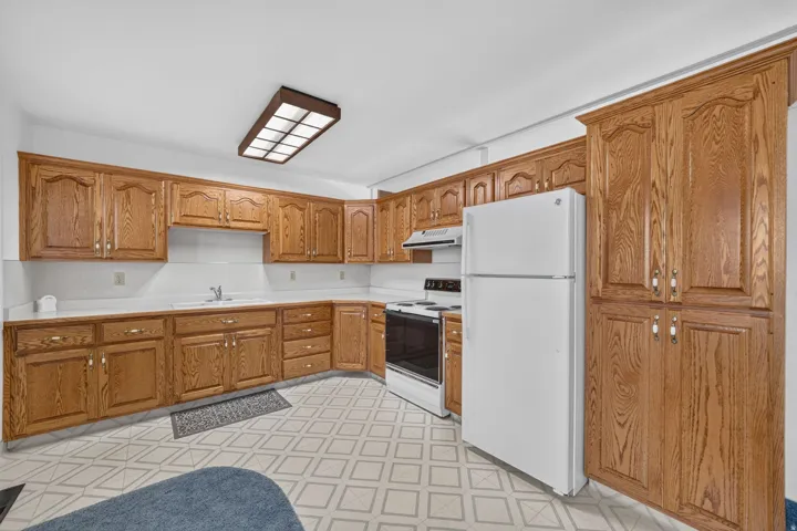Kitchen featuring extensive wood cabinetry, white countertops, a white refrigerator, a built-in oven with cooktop, and patterned flooring