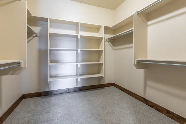Walk-in closet featuring extensive built-in shelving, multiple hanging rods, and light gray carpet flooring