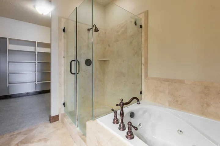 Tiled shower with glass enclosure, separate soaking tub with bronze-tone fixtures, and extensive built-in shelving