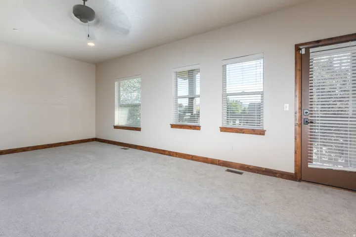 Spacious room with light gray carpet flooring, three windows with blinds, a ceiling fan, and a wood-framed glass-paneled door