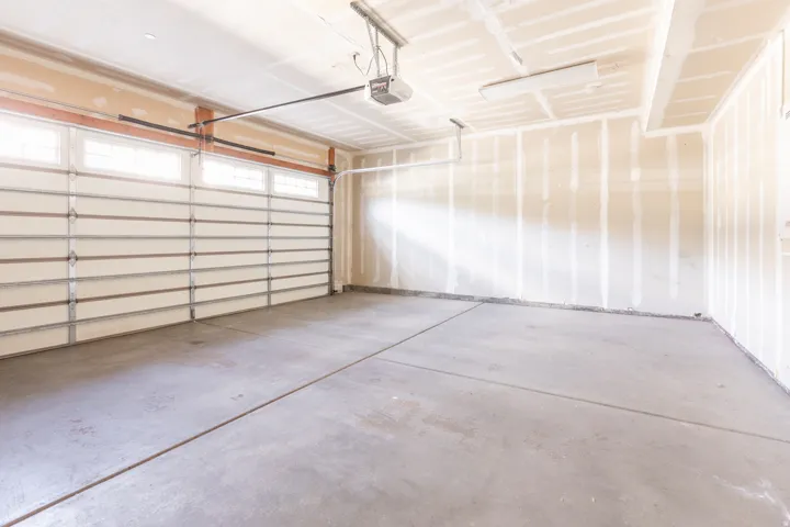 Overhead garage door with transom windows, concrete flooring, and ceiling-mounted lighting