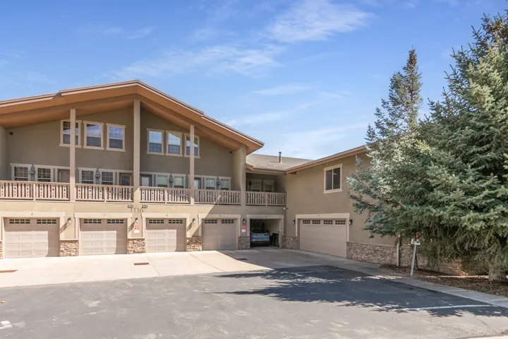 Stucco exterior with stone veneer accents, individual garage bays, multiple windows, and a raised wooden balcony