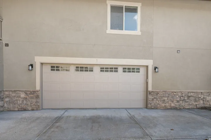 Stucco exterior featuring stacked stone accents, an overhead garage door with upper window panels, and exterior wall sconces