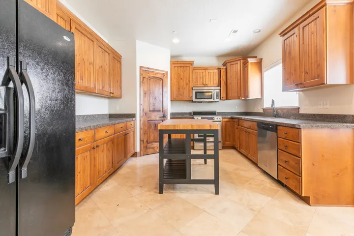 Wood cabinetry with dark countertops, a central island featuring a butcher block top, stainless steel appliances, and tile flooring