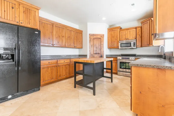 Kitchen featuring wood-finish cabinetry, granite-style countertops, stainless steel appliances, a center island with a wood butcher block top, and tiled flooring