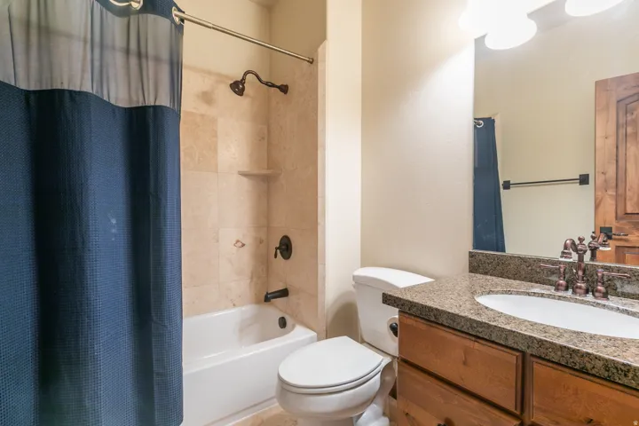 Bathroom featuring a bathtub with tiled surround, a toilet, a vanity with a counter, an undermount sink, and a framed mirror