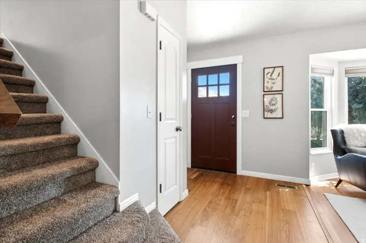 Staircase with carpeted treads, wood-finish flooring, white baseboards, and a craftsman-style entry door with glass panels
