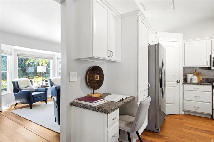 White kitchen cabinetry with stainless steel appliances, a built-in desk area with a stone-finish countertop, and wood-finish flooring