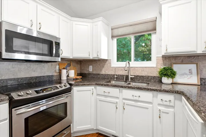 White cabinetry, stone-look countertops, stainless steel appliances, and a tile backsplash