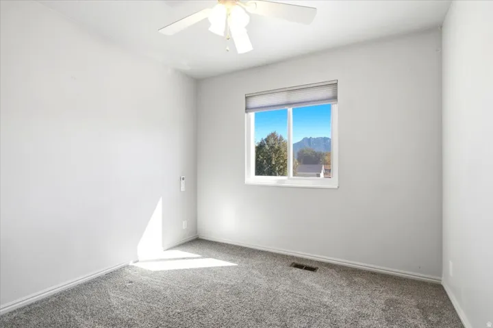 White ceiling fan with light fixture, gray plush carpeting, white walls, and a window with blinds