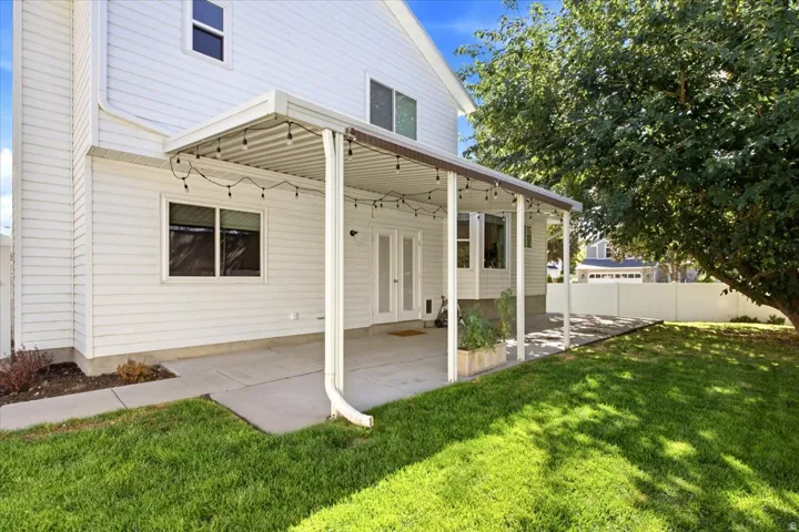 Expansive backyard featuring a covered patio, large concrete pad, mature tree, and privacy fencing