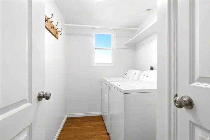 Dedicated laundry area featuring a window, built-in shelving, wood-finish flooring, and white appliances
