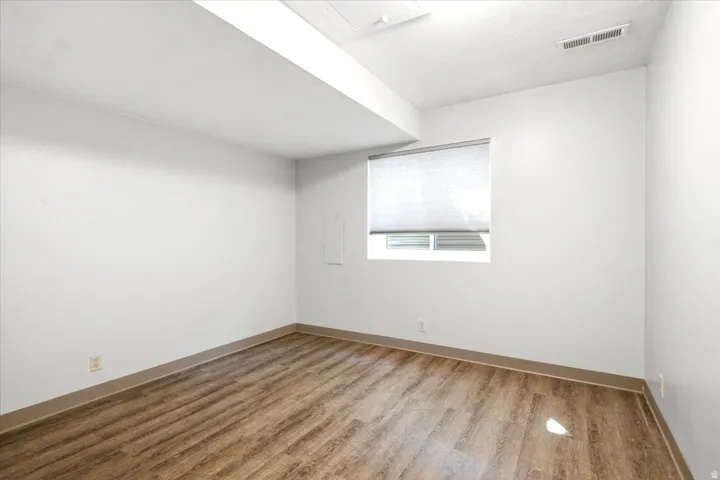 Wood-finish flooring with white walls and a window featuring a roller shade