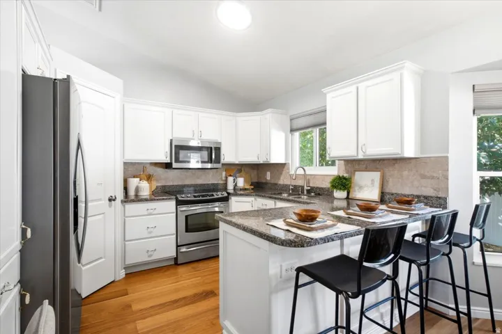 Kitchen featuring wood-finish flooring, white cabinetry, stainless steel appliances, granite countertops, and an integrated breakfast bar