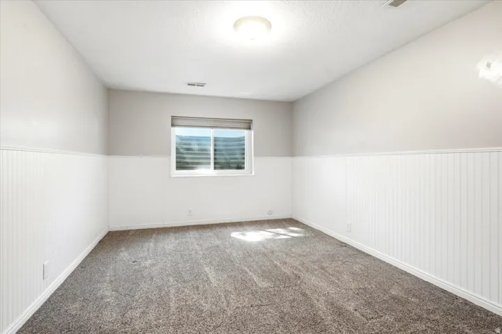 Recessed window, beadboard wainscoting, light gray wall paint, overhead light fixture, and gray textured carpeting