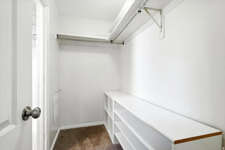 Walk-in closet featuring white built-in shelving, a garment rod, and carpet flooring