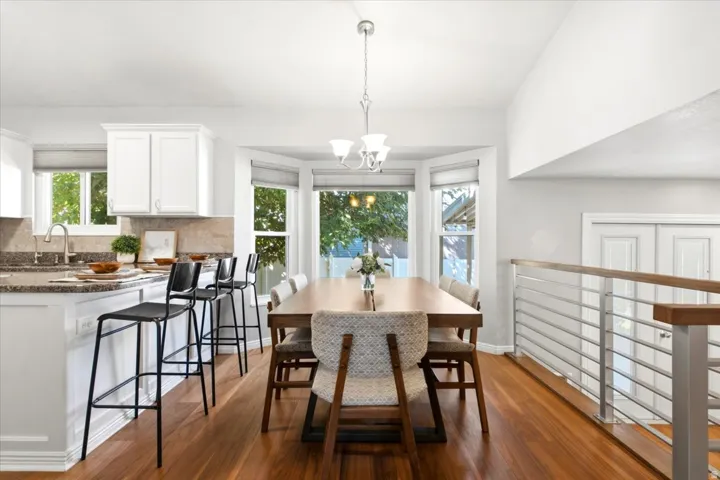 Open-concept living area featuring wood-finish flooring, white cabinetry, a kitchen island with seating, a bay window, and a modern railing system