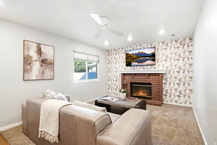 Red brick fireplace with a white mantel, ceiling fan with integrated lighting, recessed ceiling lights, and window with blinds