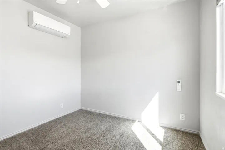 Wall-mounted air conditioning unit, ceiling fan, carpet flooring, and a single window