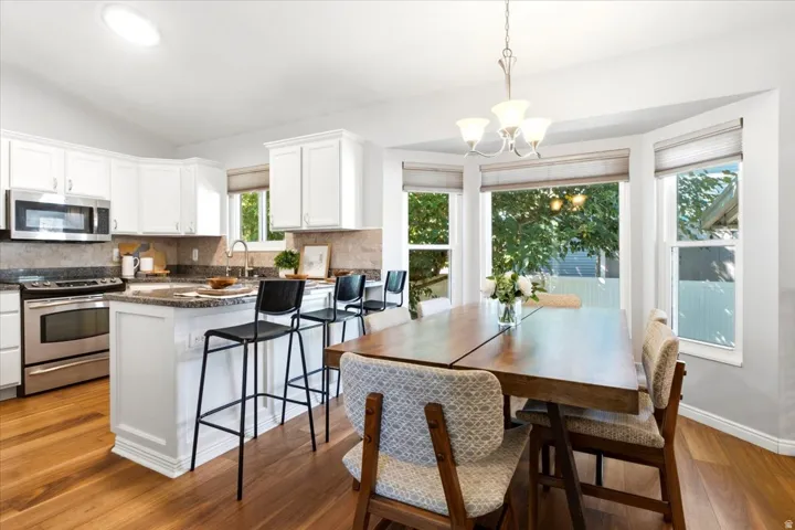 Kitchen with white cabinetry, stainless steel appliances, granite countertops, and wood-finish flooring