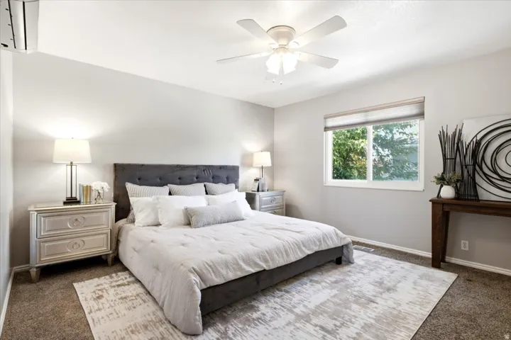 Ceiling fan, window with blinds, wall-mounted air conditioning unit, light gray wall paint, and carpeted flooring
