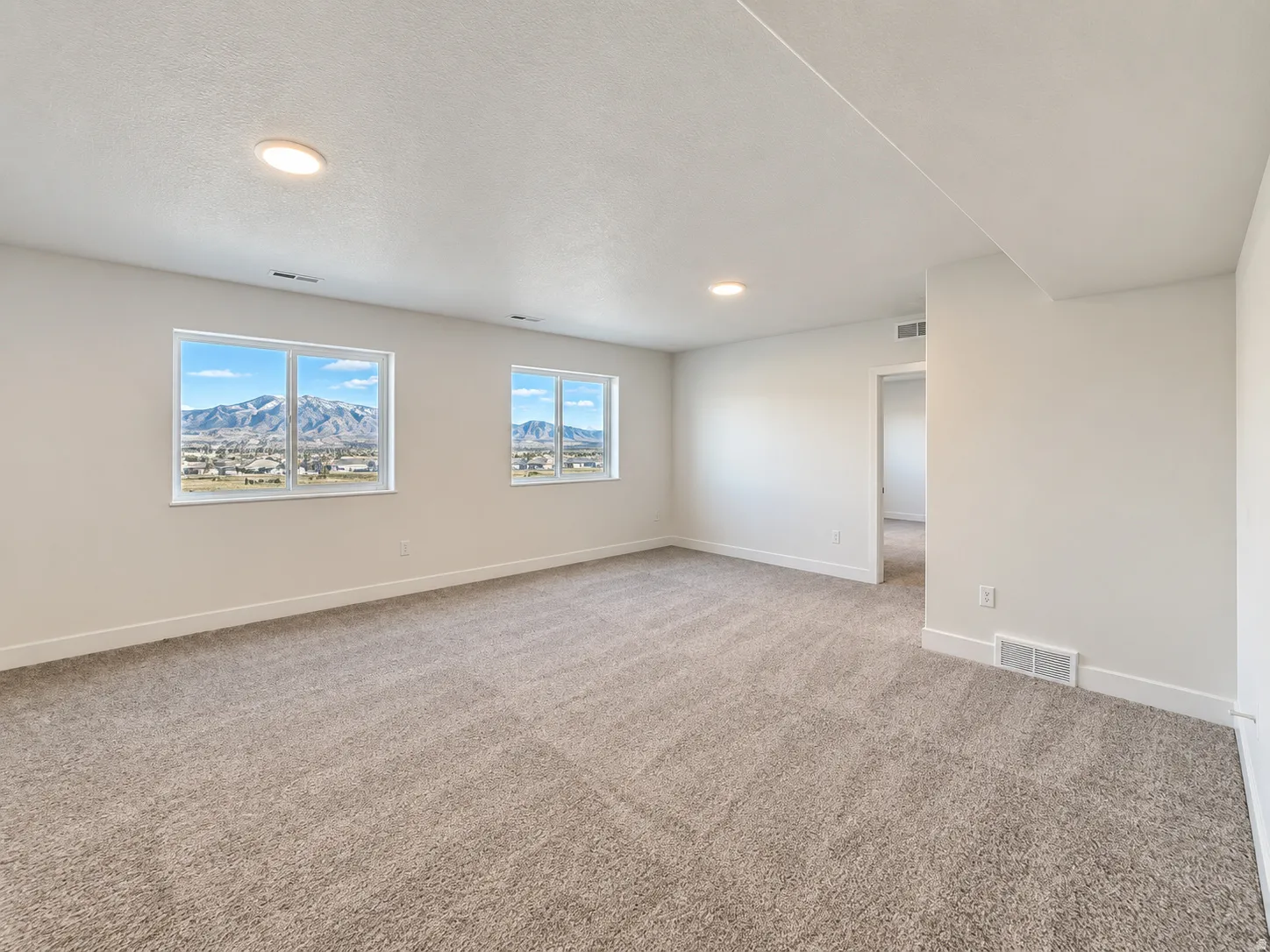 Spacious room featuring neutral carpeting, recessed lighting, and multiple windows showcasing a mountain backdrop and distant urban scenery