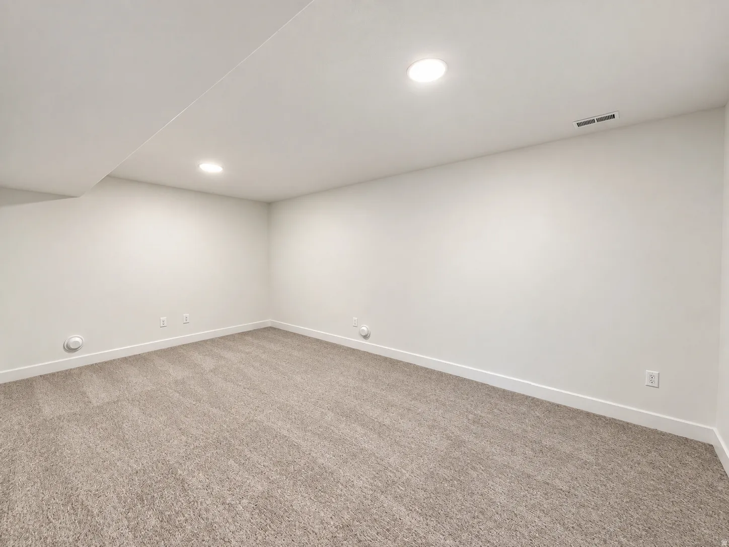 Recessed lighting illuminates the carpeted flooring and light-toned walls