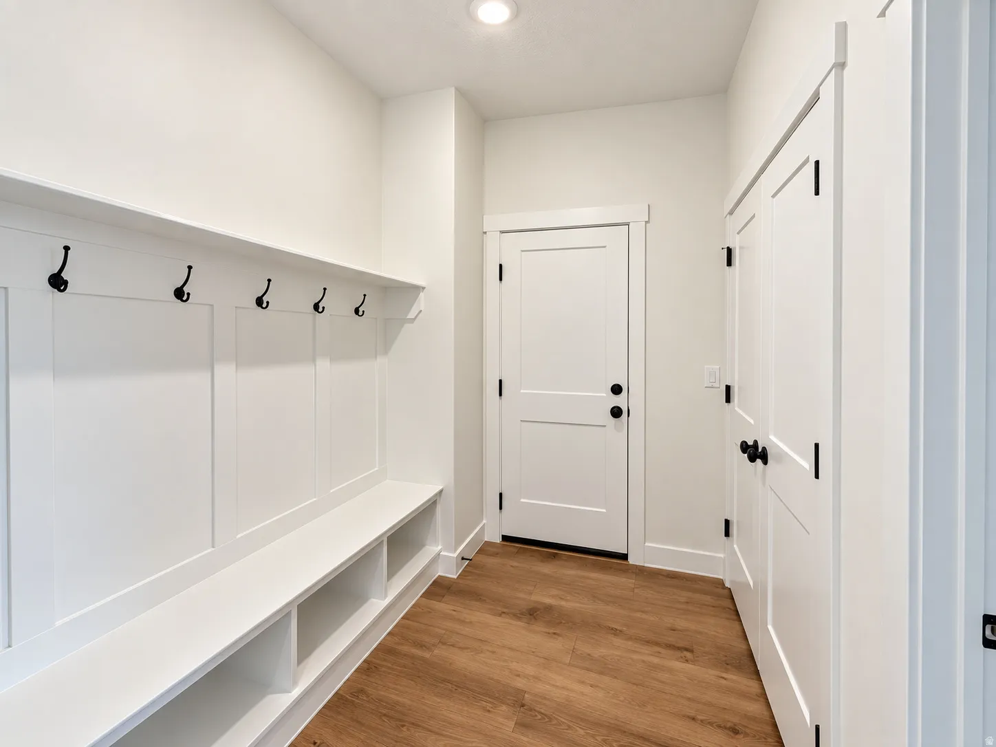 Built-in bench with storage, wall paneling, integrated coat hooks, solid white doors, and wood-finish flooring