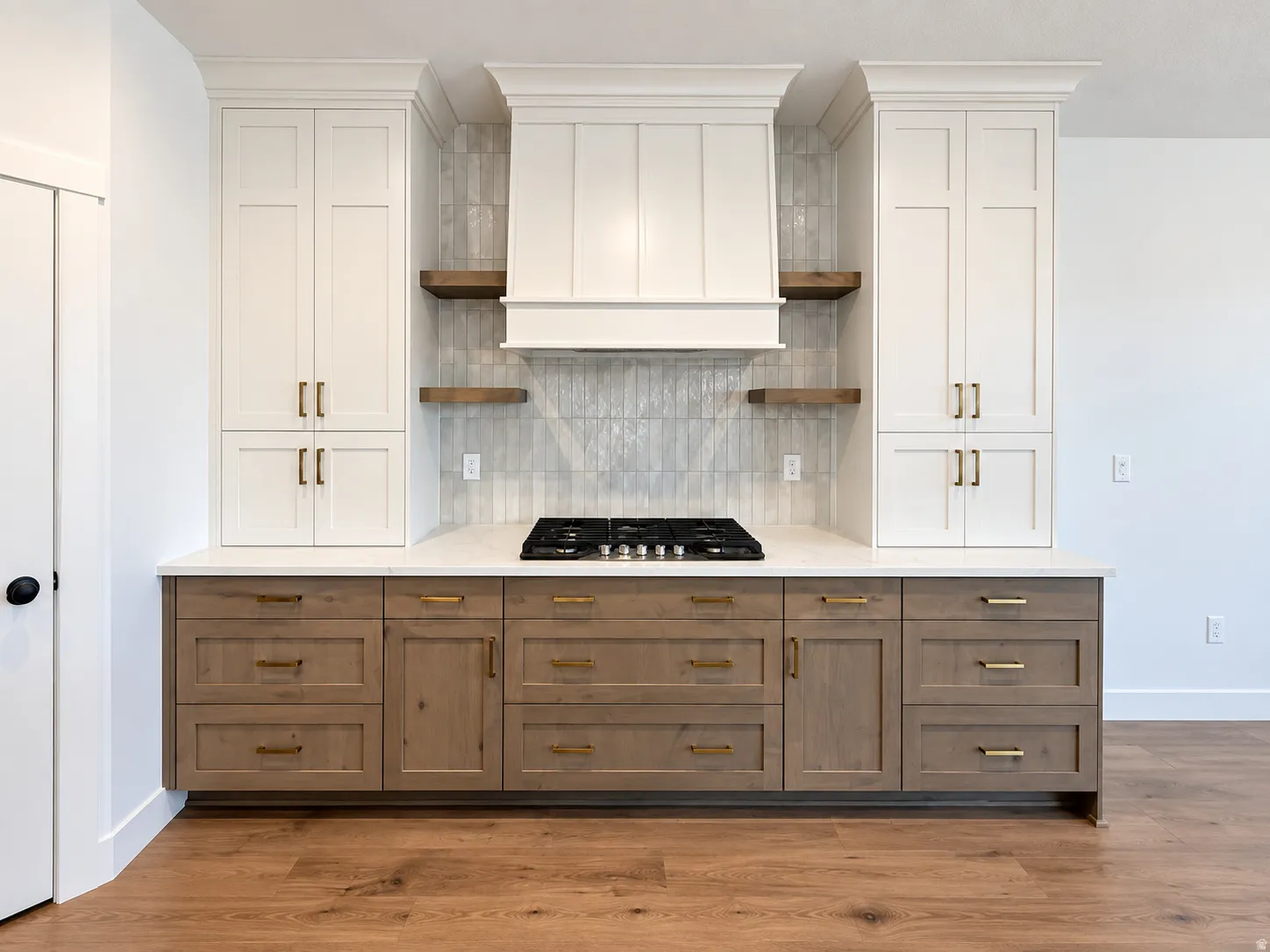 Built-in white cabinetry, wood-finish lower cabinetry, built-in gas cooktop, light-toned countertop, and wood-finish flooring