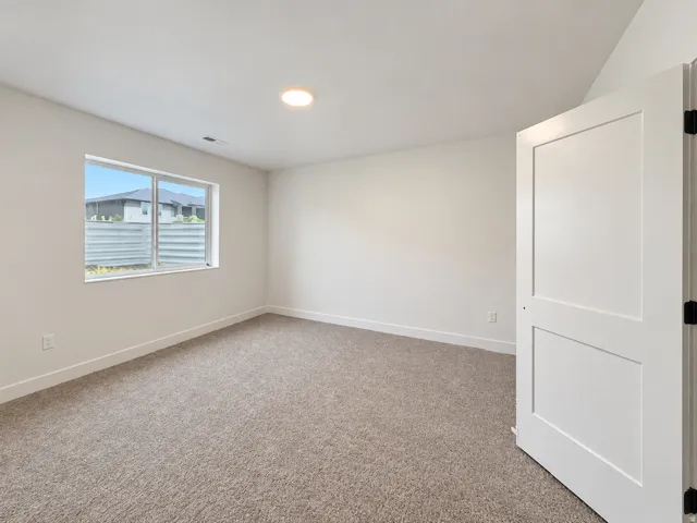 Recessed lighting, neutral carpeting, a two-panel interior door, and a single window with a window well