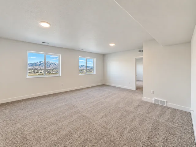 Spacious room featuring neutral carpeting, recessed lighting, and multiple windows showcasing a mountain backdrop and distant urban scenery
