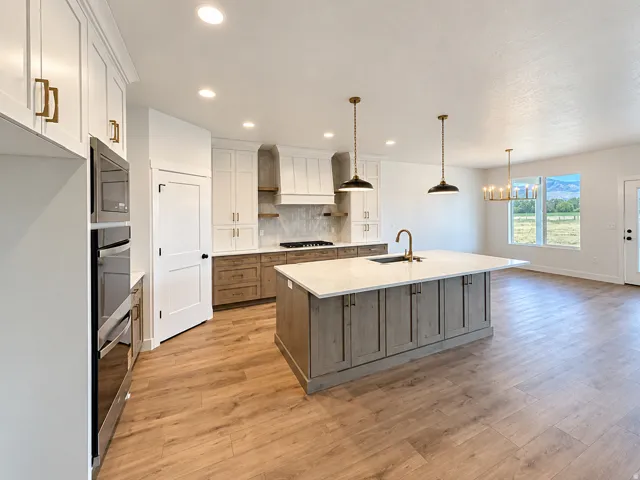 Open-concept kitchen featuring an oversized island with an undermount sink, stainless steel appliances, wood-finish flooring, white upper cabinetry, and dark wood-tone lower cabinetry
