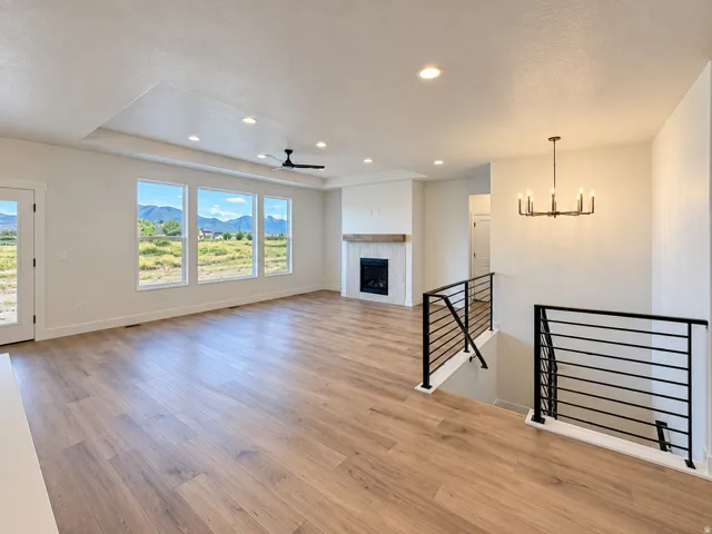 Open-concept living area featuring wood-finish flooring, a fireplace with a wood mantel, a tray ceiling with recessed lighting, and a modern chandelier