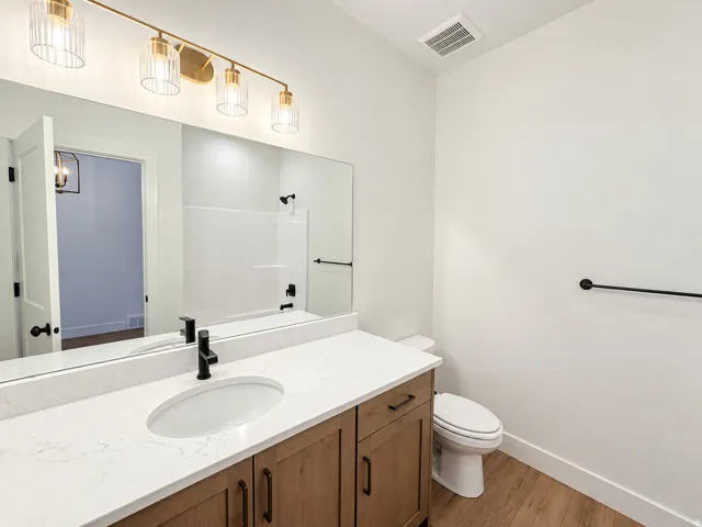 Single vanity with wood-finish cabinetry, white countertop, and matte black fixtures