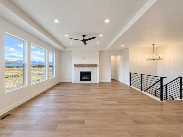 Recessed lighting, wood-finish flooring, linear fireplace with wood mantel, modern black metal staircase railing, and multiple windows