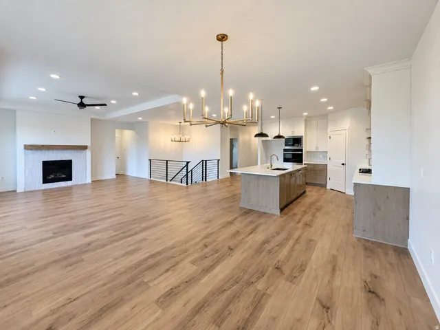 Wood-finish flooring throughout, kitchen island with built-in sink, built-in double oven, fireplace with decorative surround, and a modern staircase railing