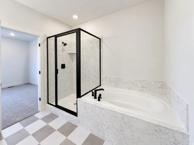 Built-in soaking tub with a stone-finish surround, walk-in shower with black-framed glass enclosure, stone-finish shower walls, and a checkered floor pattern