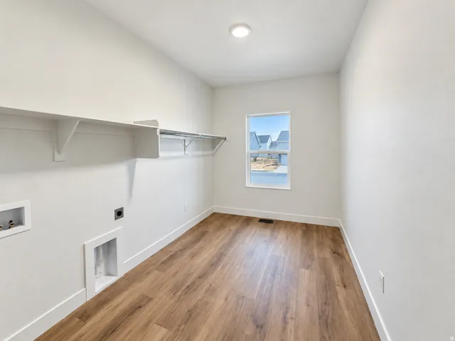 Laundry room featuring wood-finish flooring, a window, overhead shelving, and a hanging rod