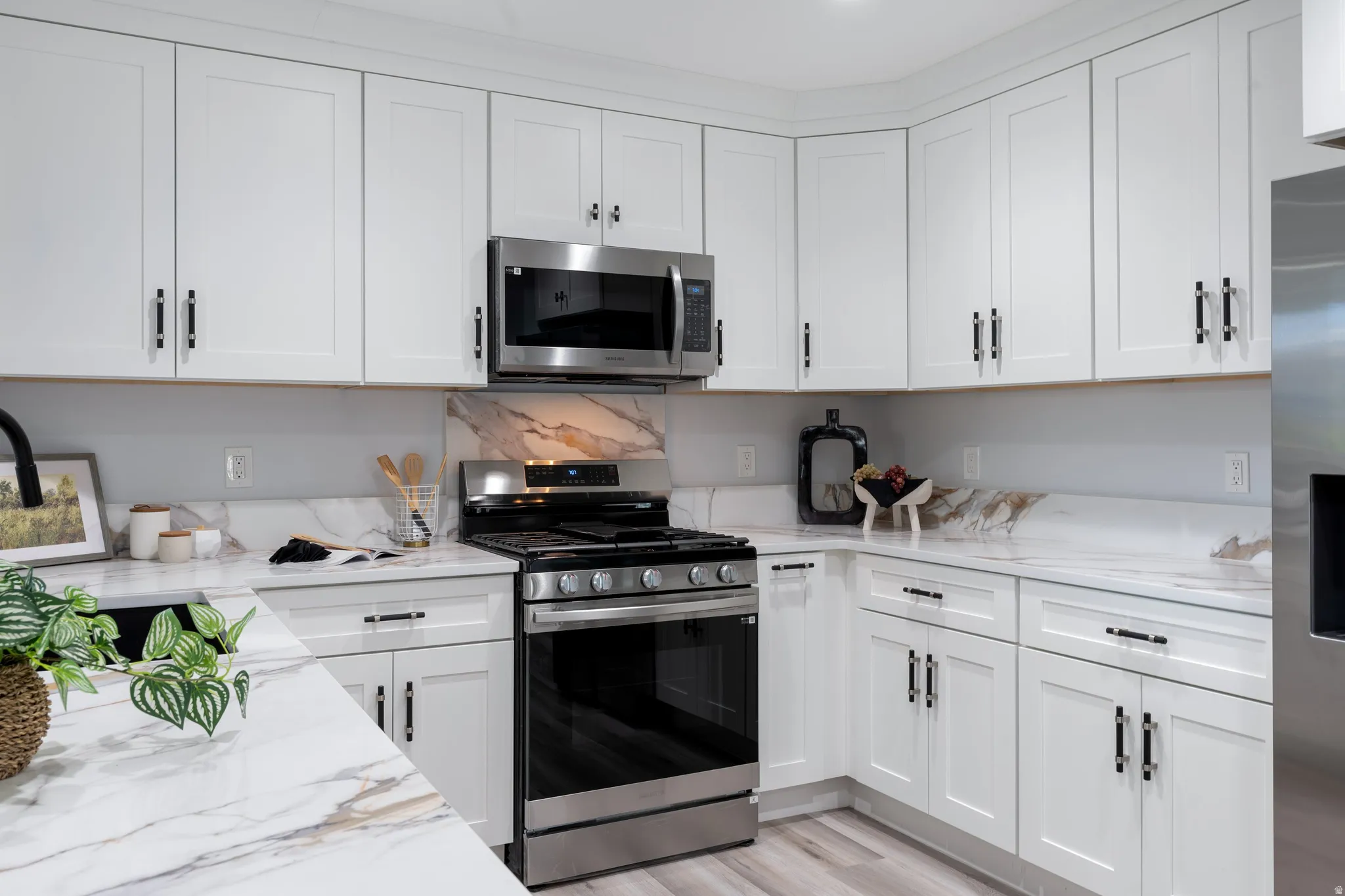 White shaker cabinetry with black hardware, stainless steel appliances, and marble-look countertops