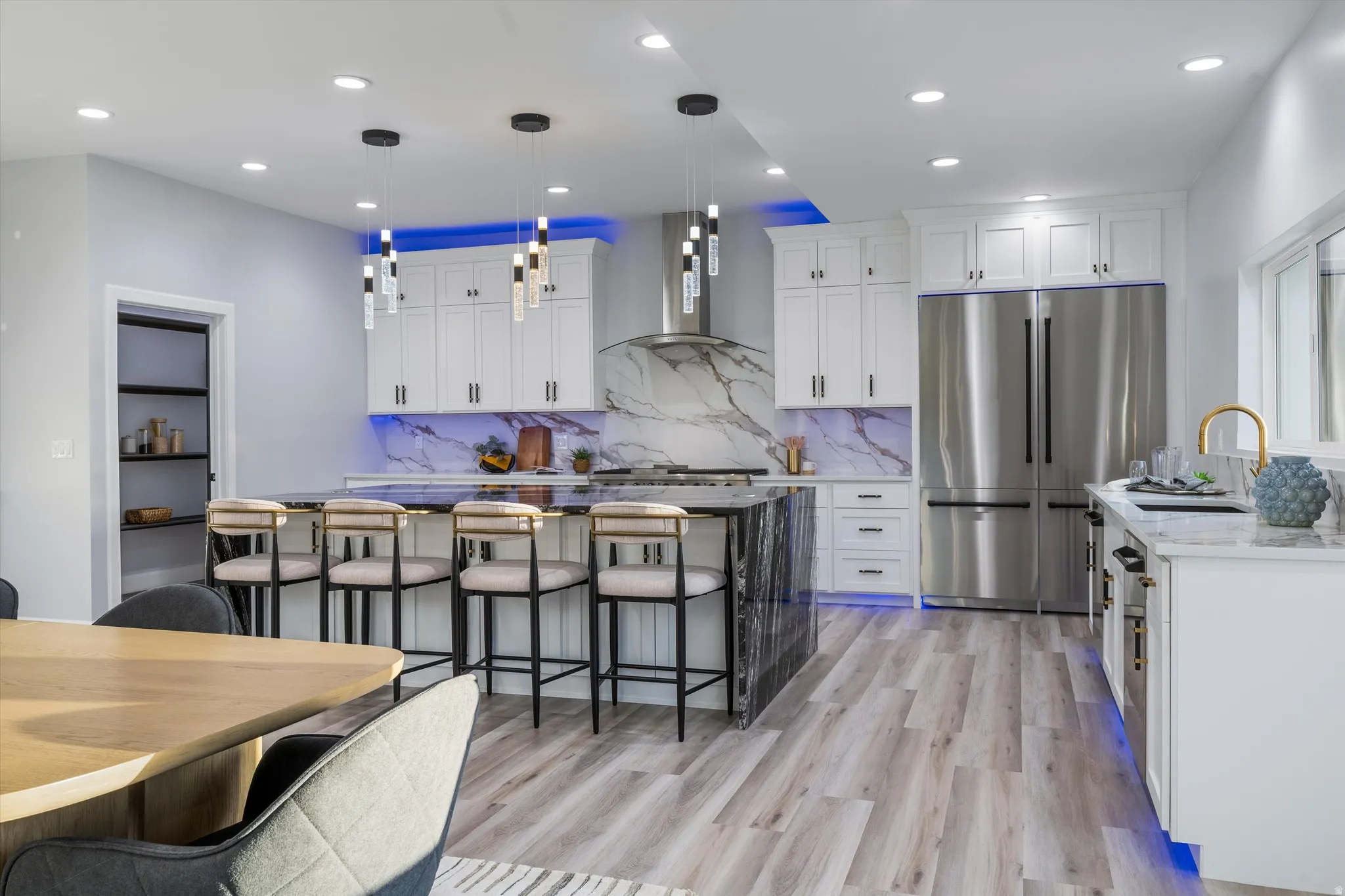 Gourmet kitchen featuring a large island, white cabinetry, integrated stainless steel appliances, marble-look backsplash, and wood-finish flooring