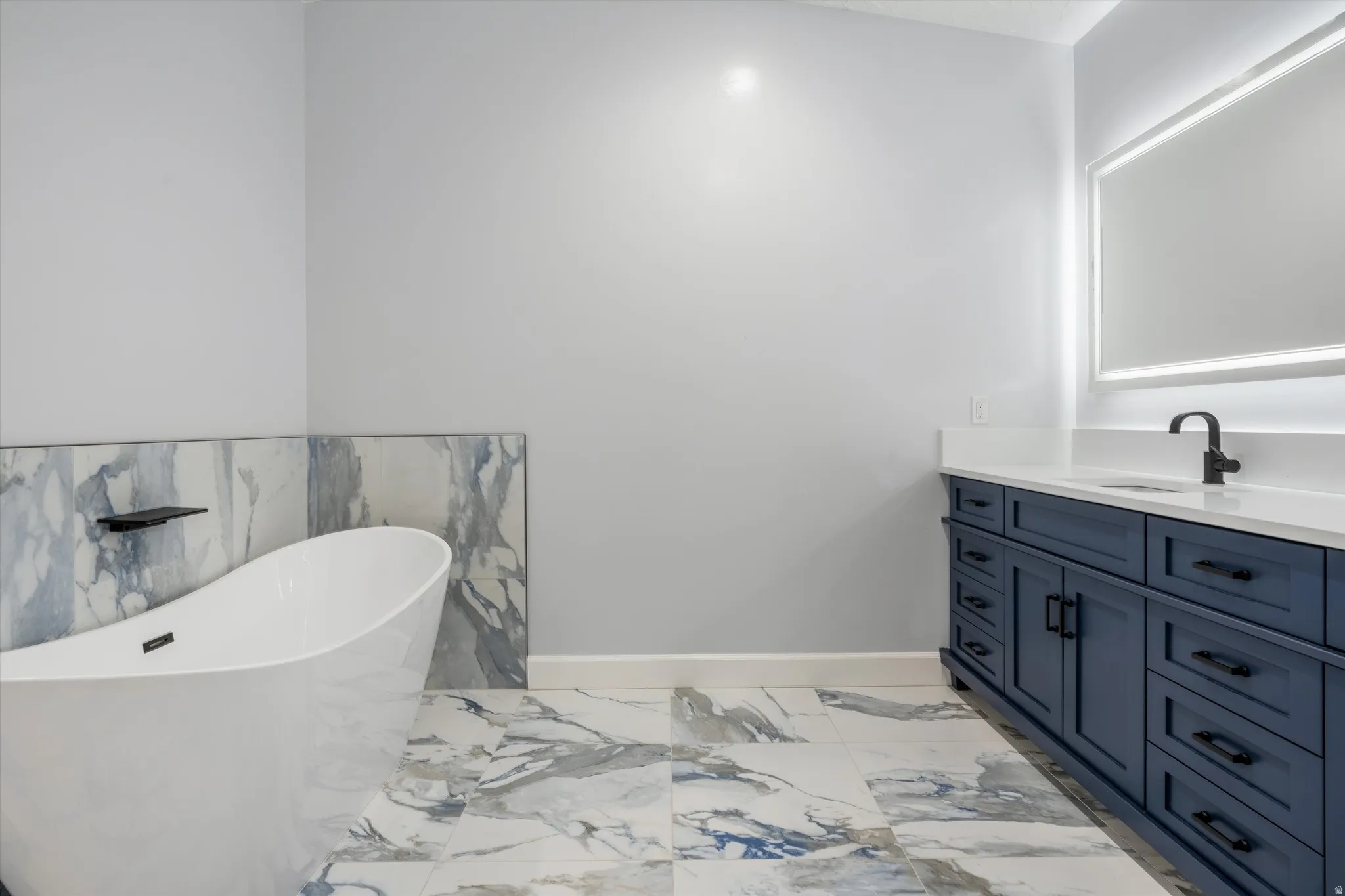 Freestanding soaking tub, blue-toned patterned tile flooring and wainscoting, and a navy blue vanity with a white countertop and matte black fixtures