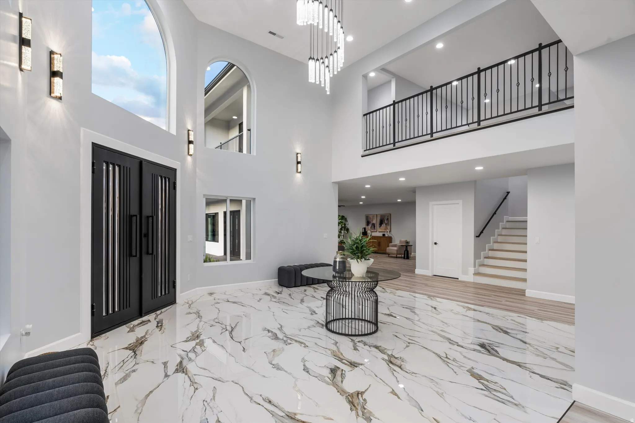Two-story foyer with a grand entry door, arched windows, a multi-tier chandelier, marble-finish flooring, and an iron baluster balcony